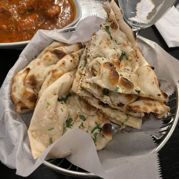 A basket of warm, fluffy Indian naan bread with cilantro, next to a bowl of curry.