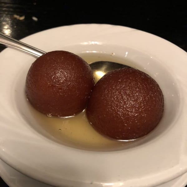 Two gulab jamun, Indian fried dough balls in syrup, served in a white bowl with a spoon.