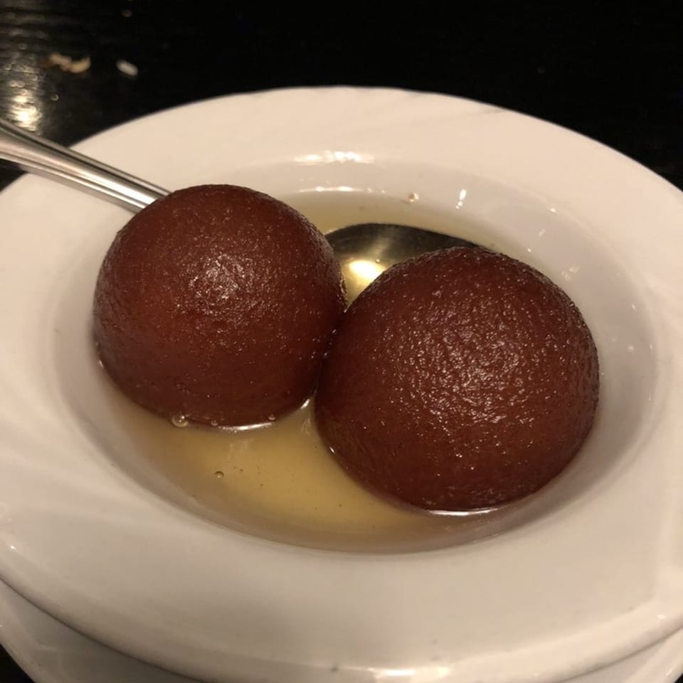 Two gulab jamun, Indian fried dough balls in syrup, served in a white bowl with a spoon.