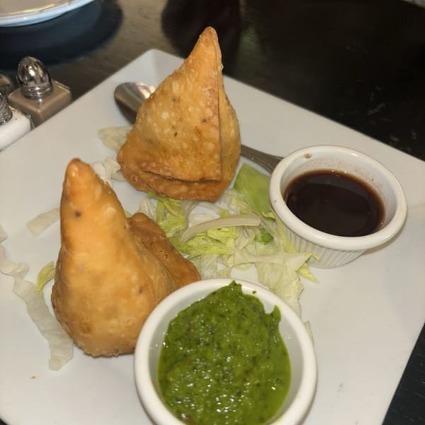 Two golden-brown samosas with green chutney and tamarind sauce on a white plate with lettuce.