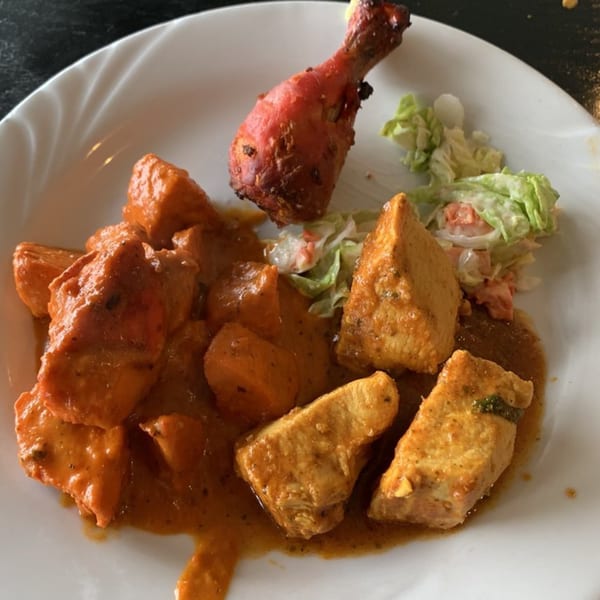 Indian dish with chicken tikka, paneer, and a drumstick, served with a side salad.