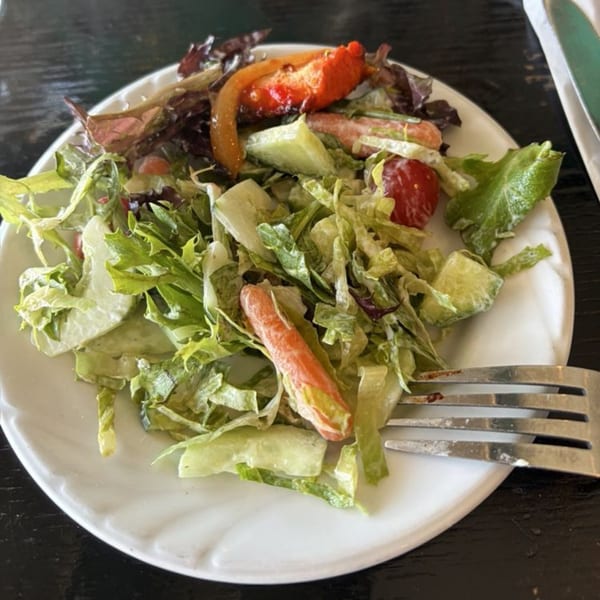 A fresh side salad with mixed greens, cucumbers, tomatoes, and carrots on a white plate.