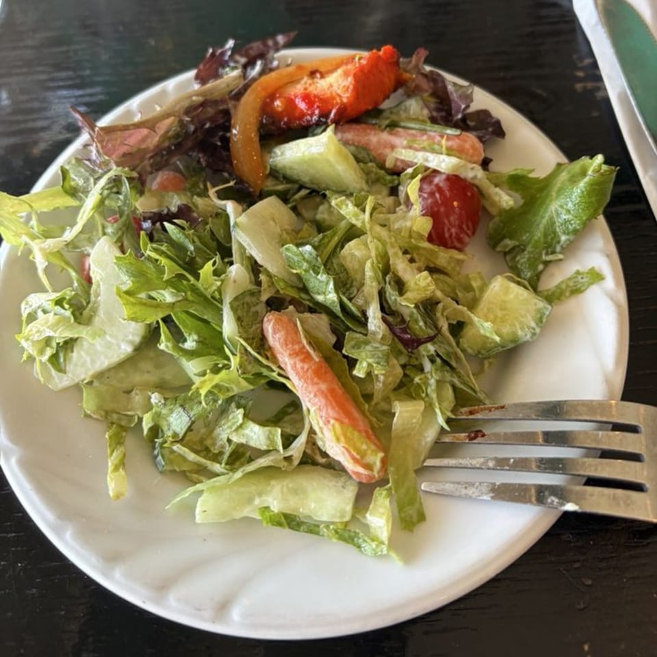 A fresh side salad with mixed greens, cucumbers, tomatoes, and carrots on a white plate.