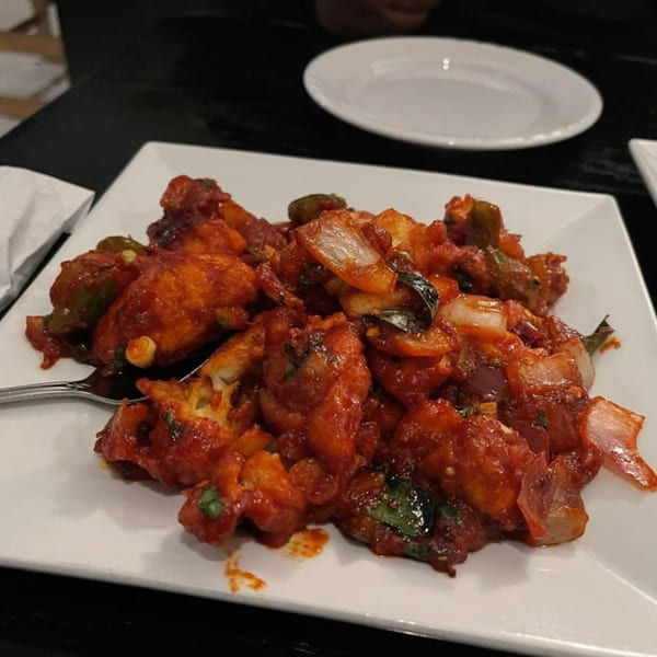 A plate of bright red Indian chili chicken with onions and green peppers.