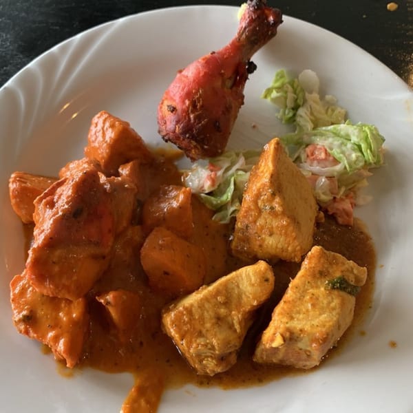A white plate with Indian butter chicken, tandoori chicken leg, and a side salad.