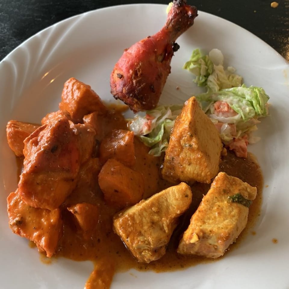 A white plate with Indian butter chicken, tandoori chicken leg, and a side salad.